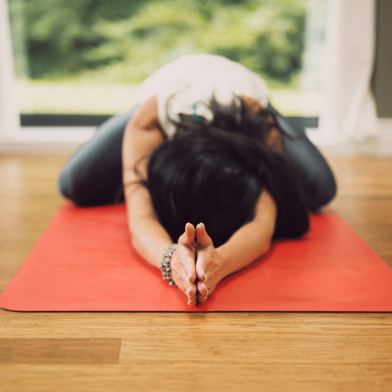 woman in white shirt lying on red mat on brown wooden table